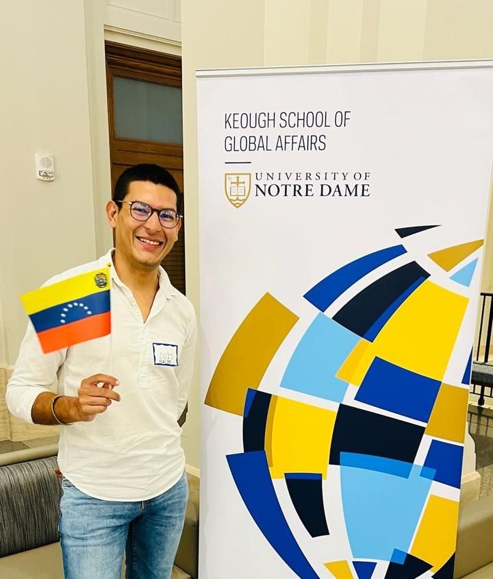 Luis Alvarado-Bruzual con la bandera de Venezuela junto al cartel de la Keough School de Notre Dame