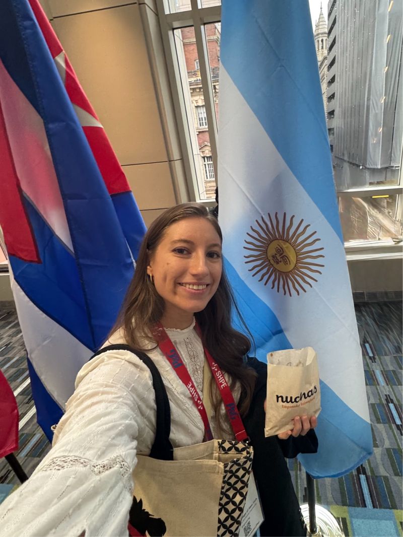Melanie Adler en una conferencia, junto a una bandera argentina